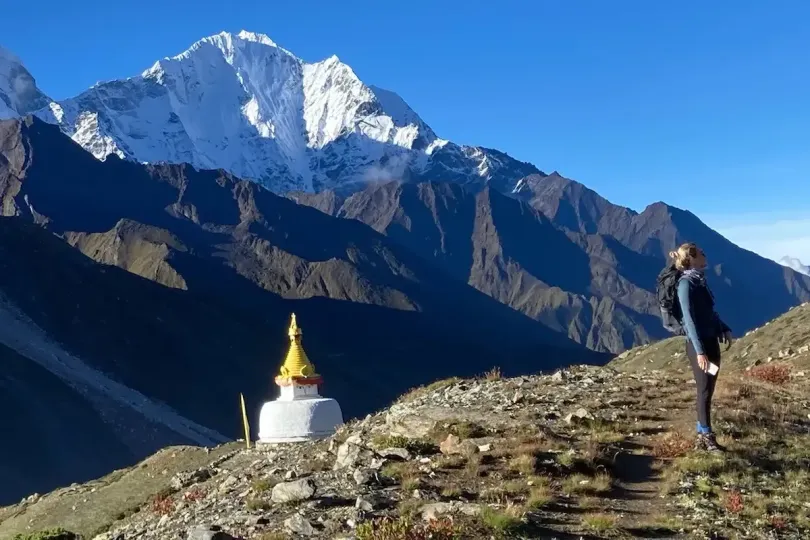Trekker standing near a Buddhist stupa on the trail above Dingboche with snowy Himalayan peaks and blue sky