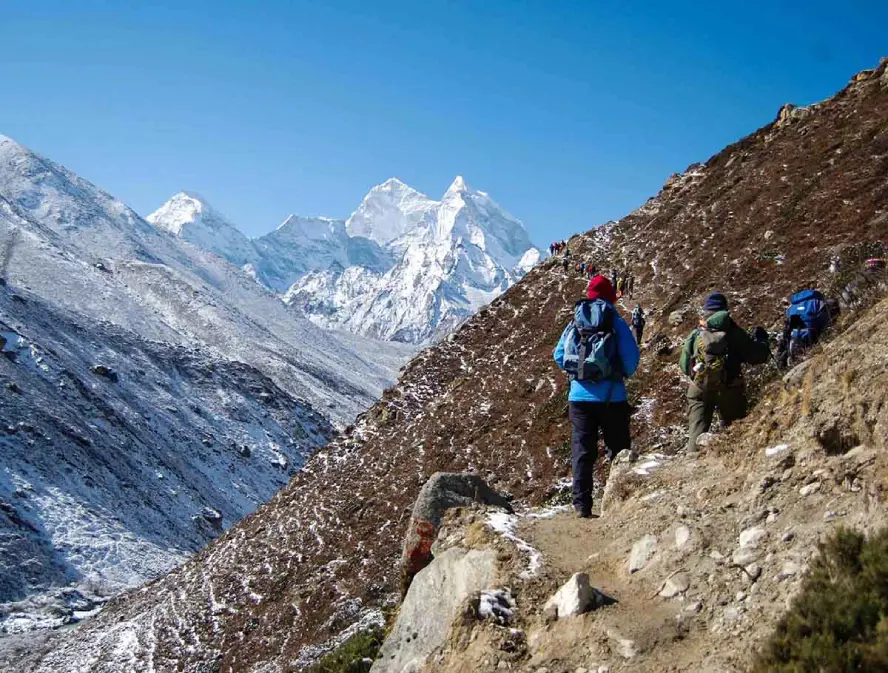 Trekkers hiking a rocky Everest Base Camp trail with snow-covered Himalayan peaks in autumn