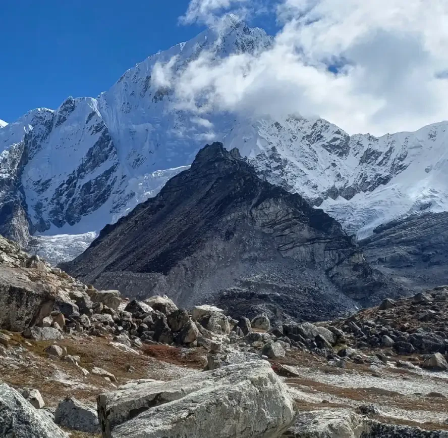 Snow-covered Himalayan mountains above a rocky glacial moraine with drifting clouds in the Everest region of Nepal.