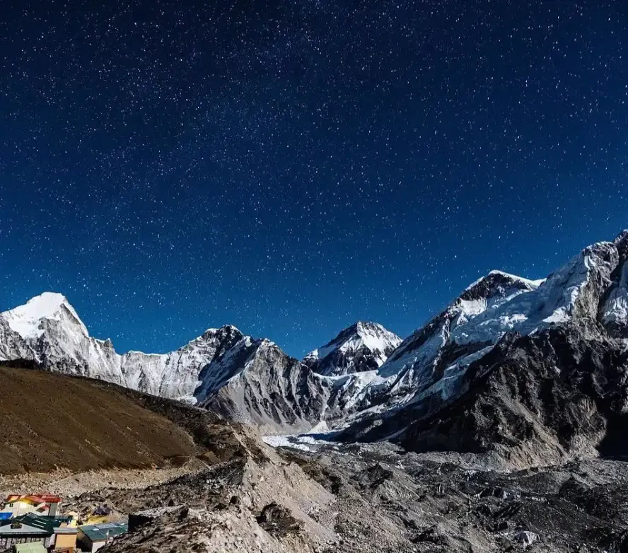 Star-filled night sky above snow-capped Himalayan peaks and glacial moraine in Nepal's Everest region.