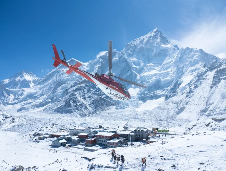 Helicopter flying over the Everest Base Camp area with snow-covered Mount Everest and trekkers below