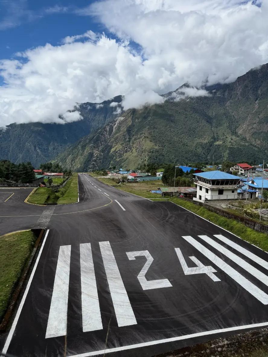 Runway 24 at Lukla Airport surrounded by lush green hills, dramatic mountain landscapes, and low-hanging clouds in Nepal's Everest region.