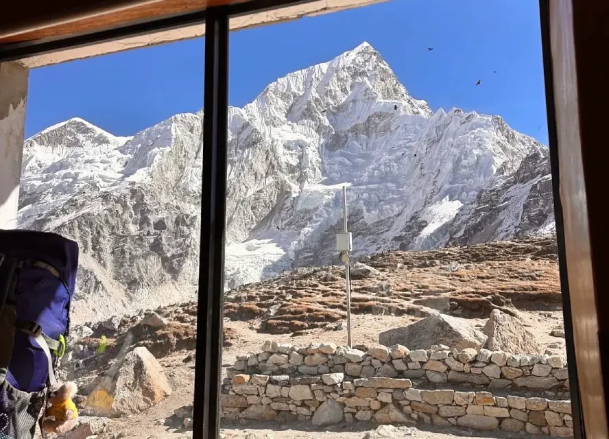 Mount Everest viewed from a lodge window near Gorak Shep with snowy Himalayan peaks and rocky trekking landscape.