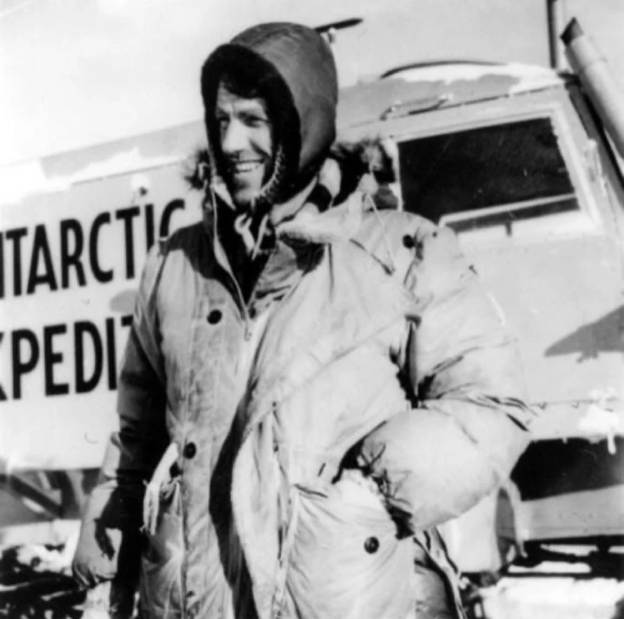 Black-and-white photograph of Sir Edmund Hillary wearing heavy polar expedition clothing and smiling beside a vehicle marked "Antarctic Expedition," capturing his pioneering exploration beyond Mount Everest.