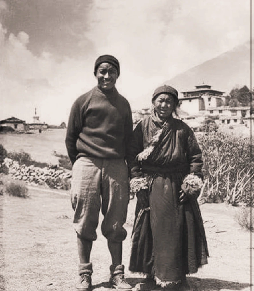 Historic black-and-white photograph of Tenzing Norgay Sherpa standing beside an elderly woman in a traditional Himalayan village, reflecting his early life and Sherpa heritage before becoming one of the first climbers to summit Mount Everest.