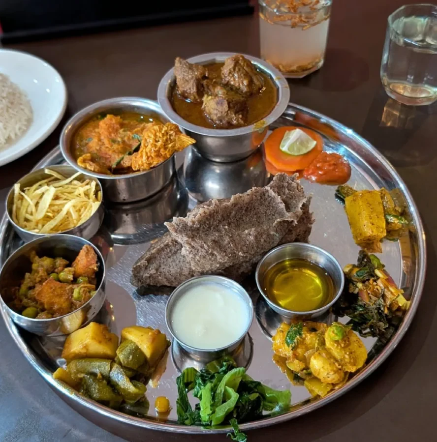 A traditional Nepali thali set served in Lukla, featuring millet dhido, meat curry, vegetable curries, yogurt, ghee, pickles, and fresh greens on a stainless steel platter, offering an authentic Himalayan dining experience.